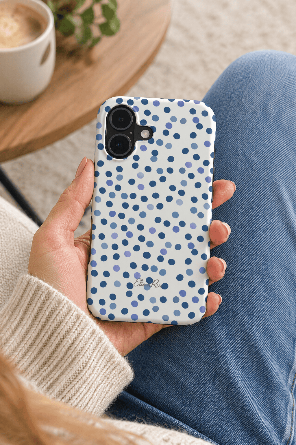 A hand holding a white phone case with a blue polka dot pattern.