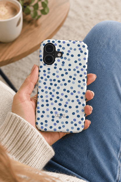 A hand holding a white phone case with a blue polka dot pattern.