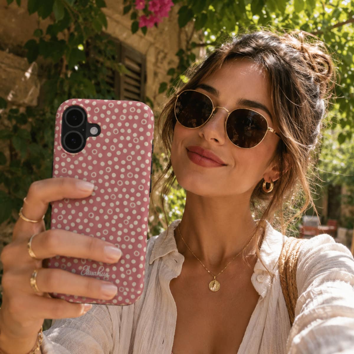 Woman taking a selfie with a phone case featuring a dusty rose polka dots pattern, wearing sunglasses and a white shirt.
