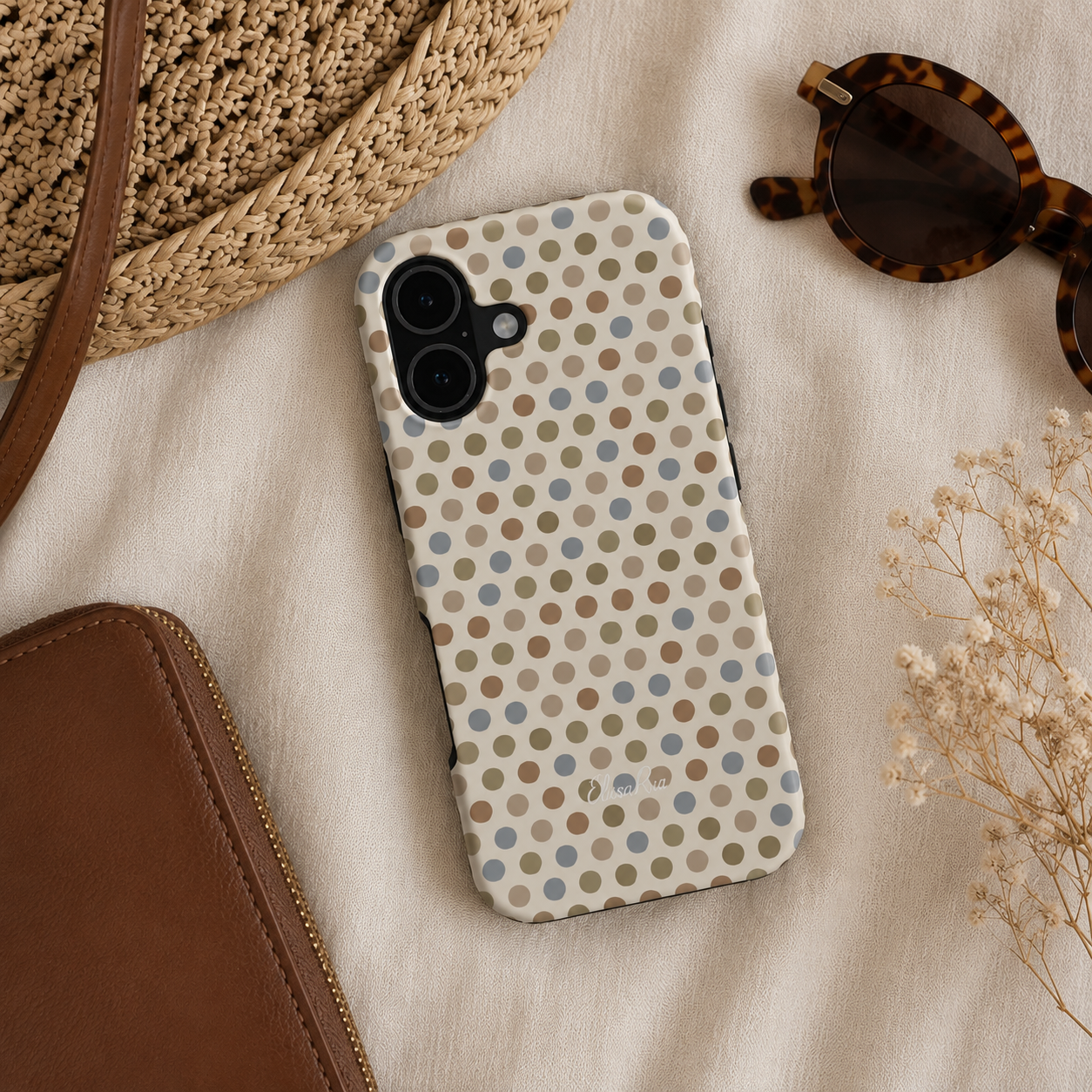 A cute phone case with a beige background and a pattern of neutral brown, tan, and light blue polka dots, styled in a flat lay.
