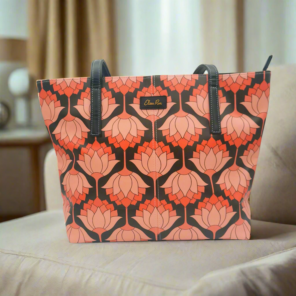 Artistic pink and black lotus tote bag placed on a beige sofa – stylish designer handbag for women by Elissa Rua.