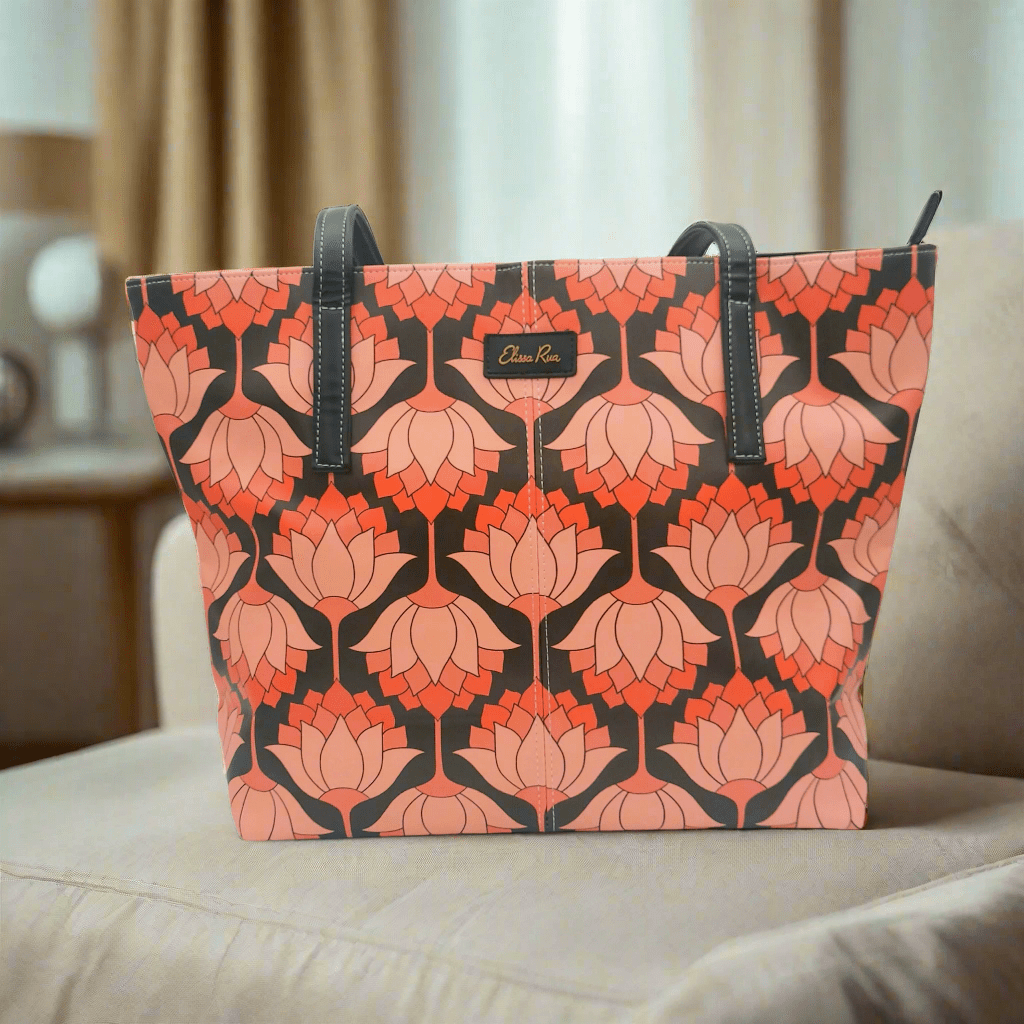 Artistic pink and black lotus tote bag placed on a beige sofa – stylish designer handbag for women by Elissa Rua.